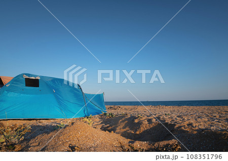 Tent, summer camping on the beach, against the backdrop of the sea and sky. A bright blue large tent stands on the sandy shore, no one 108351796