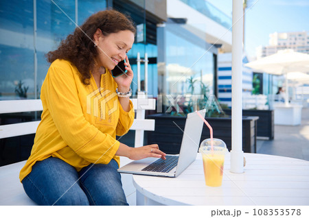 Middle Eastern business woman talking on mobile phone, working on laptop, dealing with current projects for work online Middle Eastern business woman talking on mobile phone, working on laptop, dealing with current projects for work online 108353578