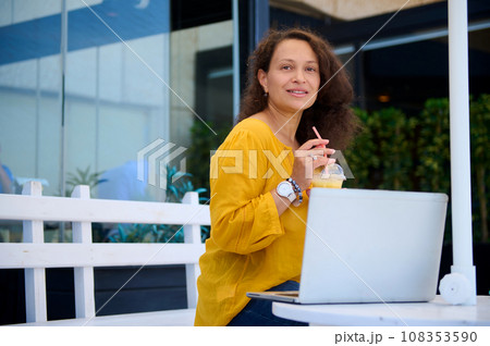 Happy successful middle aged woman, entrepreneur drinking freshly squeezed juice and working online on laptop in a cafe 108353590