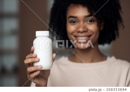 Food supplement. Young African American woman holding a white jar bottle of vitamins or pills. Place for your logo 108353694
