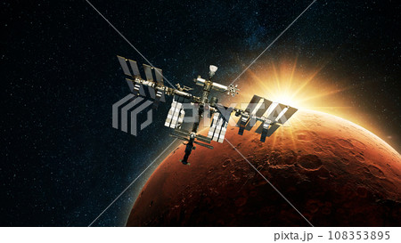ISS spacecraft flies against the backdrop of dawn light and red planet Mars with craters in deep space. Journey to Mars, concept 108353895
