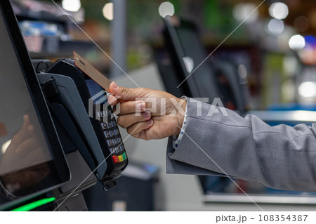 Close-up photo of the hand of a female buyer paying in a supermarket store with a bank credit card at the self-service checkout. 108354387