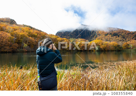 旅行先で秋の池の景色をカメラで撮影している中高年男性 旅行先で秋の池の景色をカメラで撮影している中高年男性 108355840