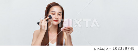 Banner of beautiful young woman holding makeup brush isolated over white background 108359749
