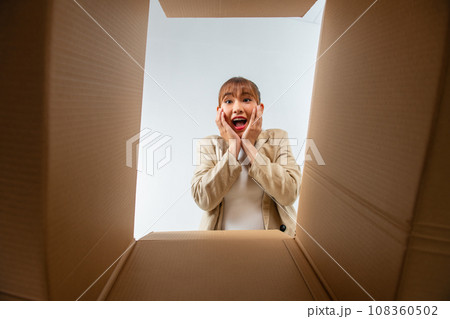A young woman opens up a box, surprised and happy to see their order better than expected A young woman opens up a box, surprised and happy to see their order better than expected 108360502