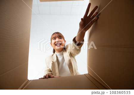 Happy laughing young woman putting arms into box, feeling excited receiving order from internet store 108360535