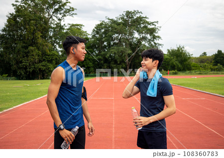 Two Asia male Athlete Drinking Water talking wiping face on Track together Two Asia male Athlete Drinking Water talking wiping face on Track together 108360783