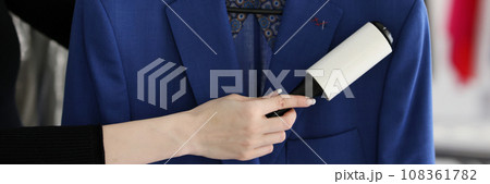 Woman removes pellets from blue woolen coat with roller 108361782