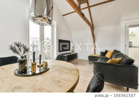 a living room with wood flooring and white walls, including a round wooden table surrounded by black leather chairs 108362587