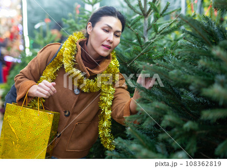 Happy asian woman chooses Christmas tree on street market Happy asian woman chooses Christmas tree on street market 108362819