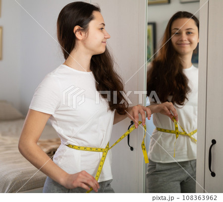 Young pretty girl with measuring tape at bedroom Young pretty girl with measuring tape at bedroom 108363962