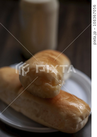 Bread on a white plate sits on a wooden board table with milk in a bottle behind it Bread on a white plate sits on a wooden board table with milk in a bottle behind it 108367056