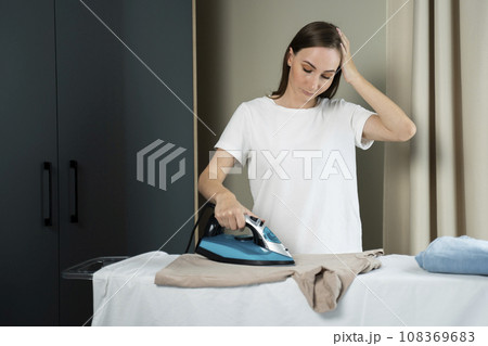 Tired housewife irons clothes on an ironing board. Tired woman housewife ironing clothes iron in laundry 108369683