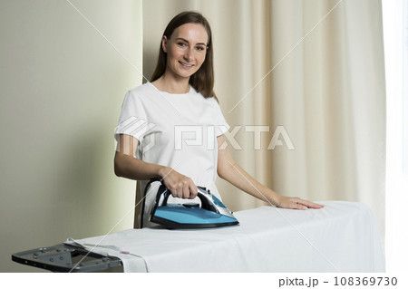 The concept of people, housework, laundry and housekeeping - a happy woman ironing bed linen on an ironing board at home The concept of people, housework, laundry and housekeeping - a happy woman ironing bed linen on an ironing board at home 108369730