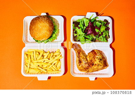 Opened paper box with salad with baked chicken against hamburger with fried potato over orange-green background. Concept of fast food, delivery. 108370818