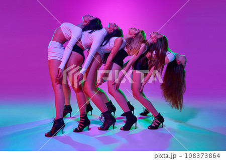 Group of artistic, young, elegant omen performing, dancing high heel dance over pink studio background in neon light 108373864