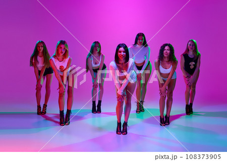 Group of beautiful women dance high heel dance, training over pink studio background in neon light 108373905