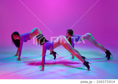 Beautiful, artistic, elegant women with slim bodies dancing high heel dance over pink studio background in neon light 108373914