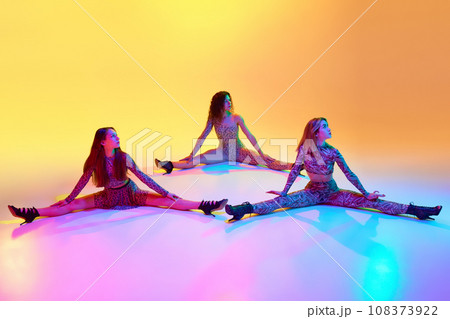 On twine. Young beautiful women dancing high heel dance, training over gradient yellow background in neon light On twine. Young beautiful women dancing high heel dance, training over gradient yellow background in neon light 108373922
