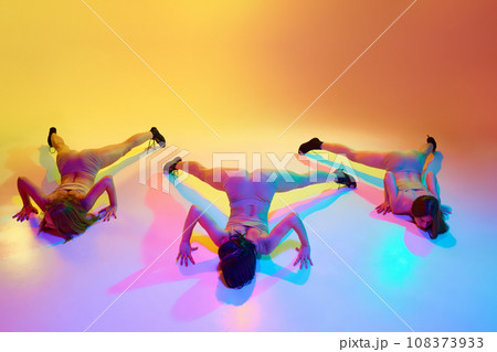 Freedom of movements. Three young woman in underwear dancing high heel dance on floor over gradient yellow background in neon light Freedom of movements. Three young woman in underwear dancing high heel dance on floor over gradient yellow background in neon light 108373933