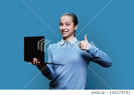 Serious teenage student girl using laptop on blue background, showing finger up 108374191