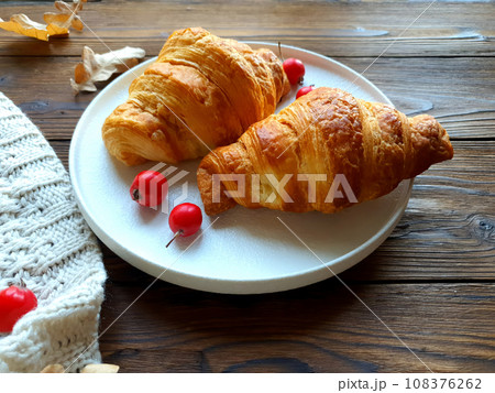 There is a plate with freshly baked croissants on the wooden table. 108376262