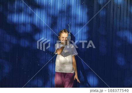 Sunny Splashes: Teenage Girl Radiates Joy Against a Vivid Blue Wall 108377540