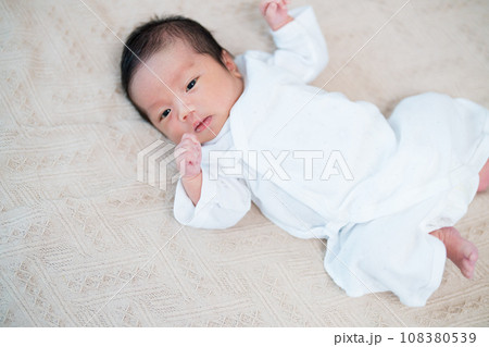 リビングのソファで寝転がってうとうと眠そうにしている生まれたての赤ちゃん 108380539