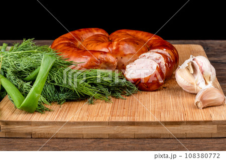Sliced homemade fried sausage on a wooden cutting board and garlic with herbs. 108380772
