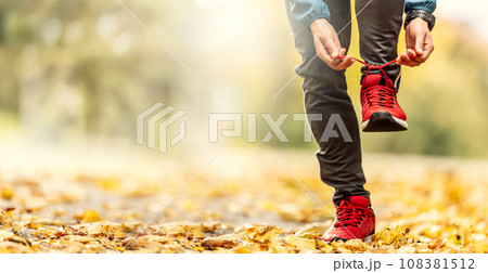 A close-up view of the hands of an athlete tying his shoelaces before running in an autumn park A close-up view of the hands of an athlete tying his shoelaces before running in an autumn park 108381512
