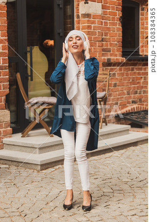 Middle eastern woman in hijab listening music with headphones and dancing outdoors. Woman independence and feminism concept. 108384365