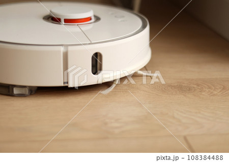 Wireless autonomous smart robotic vacuum cleaner is vacuuming floor with modern tiles at living room. Self-propelled cleaning robot. Floor cleaning system. Household remote control appliances. 108384488