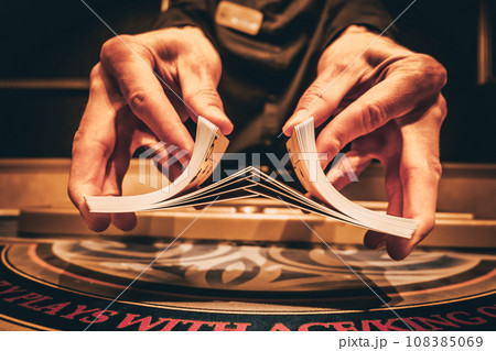 Dealer or croupier shuffles poker cards in a casino on the background of a table, chips. Concept of poker game, game business. Playing for money, a big win, a jackpot, gambling, a desire to get rich. Dealer or croupier shuffles poker cards in a casino on the background of a table, chips. Concept of poker game, game business. Playing for money, a big win, a jackpot, gambling, a desire to get rich. 108385069