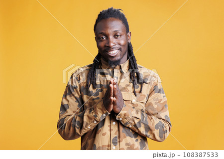 Happy african american person holding palms together, asking for something in studio over yellow background. Smiling man celebrating succes, applauding people after work achievement Happy african american person holding palms together, asking for something in studio over yellow background. Smiling man celebrating succes, applauding people after work achievement 108387533