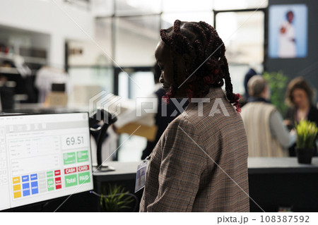 Showroom employee analyzing merchandise inventory on computer, working at clients purchase report in shopping centre. African american worker standing at cash register in modern boutique 108387592