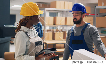 Multiethnic team of workers scanning merchandise barcodes, looking at products packed in cardboard boxes. Male employee bringing goods in package to supervisor, planning shipment. 108387624