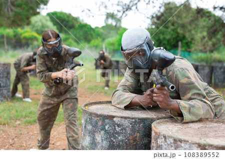 African american man paintball player aiming and shooting with gun at opposing team African american man paintball player aiming and shooting with gun at opposing team 108389552