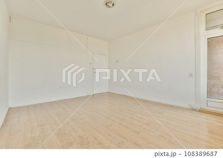 an empty room with white walls and wood flooring on the right, there is a brick wall in the background 108389687