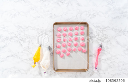 Piping meringue from the piping bags with the metal tip into parchment paper to bake meringue cookies. 108392206