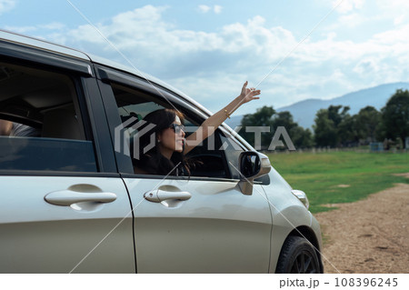 Smiling female driving vehicle on the road on a bright day. Sticking her head out the windshield 108396245