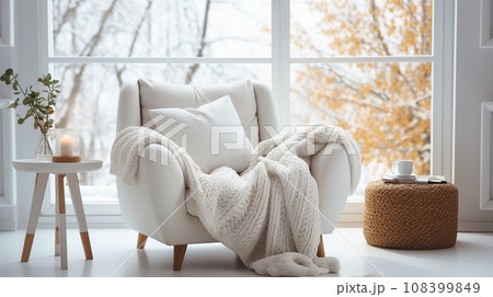 A cozy light soft chair with knitted blanket and coffee table with vase against backdrop of large stained glass window 108399849