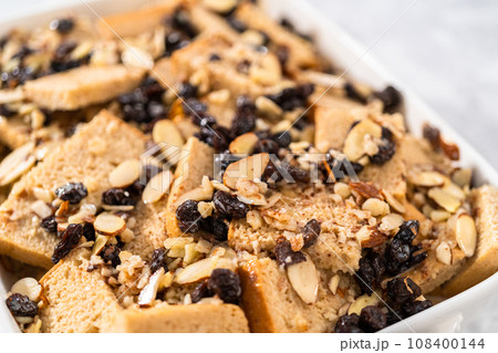 Baking bread pudding with raising and almond slivers in a white casserole dish. Baking bread pudding with raising and almond slivers in a white casserole dish. 108400144