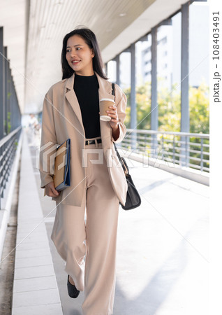 A confident Asian businesswoman is walking on the skywalk in the city with her stuff. 108403491