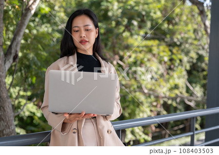 A busy, professional Asian businesswoman is working on her laptop outdoors on the skywalk. A busy, professional Asian businesswoman is working on her laptop outdoors on the skywalk. 108403503