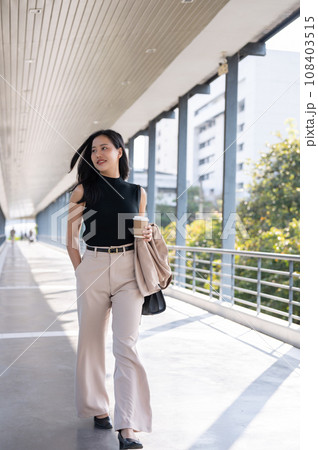 A confident and gorgeous Asian businesswoman or female CEO is walking on a skywalk or footbridge. 108403515