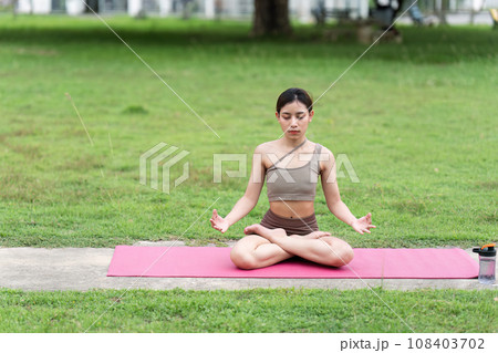 Asian woman in sporty outfit relaxing meditating feeling zen like on fitness mat in public park outdoor. Healthy active lifestyle 108403702