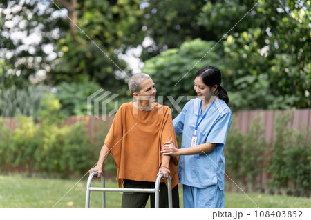 Nurse or caregiver help elderly walk by using walker in garden 108403852