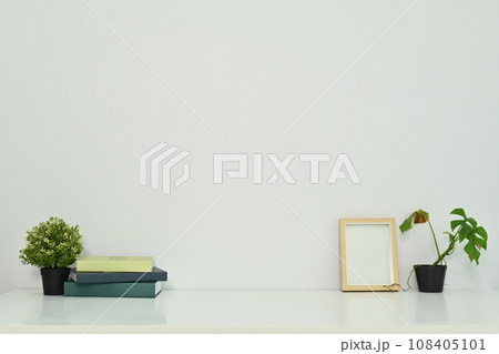 Minimal workplace with books, coffee cup, photo frame and potted plants on table against a clean white wall Minimal workplace with books, coffee cup, photo frame and potted plants on table against a clean white wall 108405101