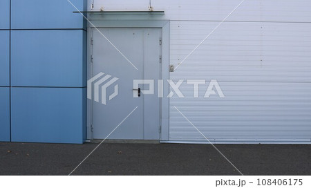 wall of a building made of gray and blue panels with a closed door as an urban abstract texture background with copy space, a side exit from a store or supermarket as an urban space without people 108406175