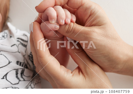 Parents' hands hold the fingers of a newborn baby. The hand of a mother and father close-up holds the fist of a newborn baby. Family health and medical care. Professional photo on white background 108407759